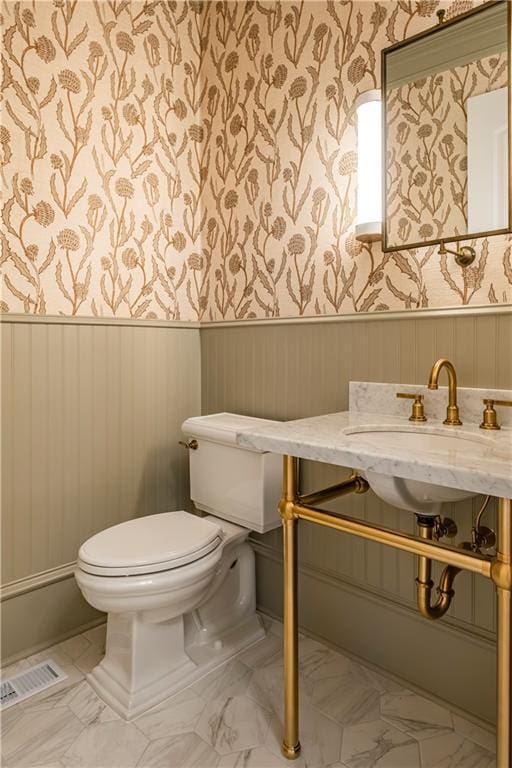 bathroom with toilet, wallpapered walls, visible vents, and a wainscoted wall