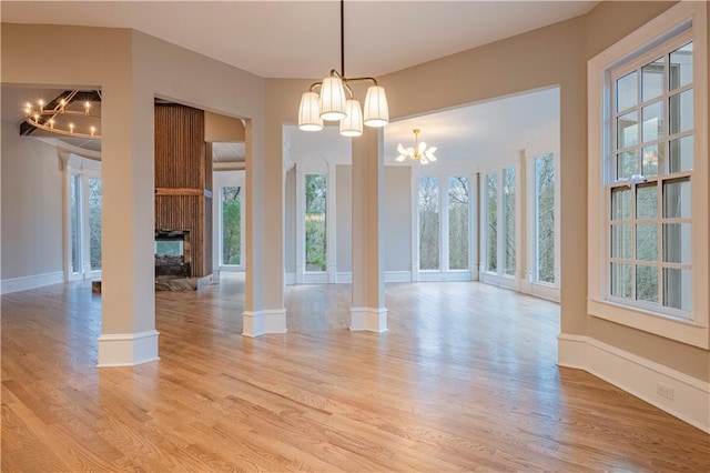 unfurnished dining area with a notable chandelier, light wood-style flooring, a multi sided fireplace, baseboards, and ornate columns
