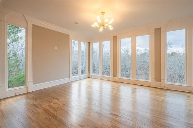 spare room featuring crown molding, an inviting chandelier, wood finished floors, and visible vents
