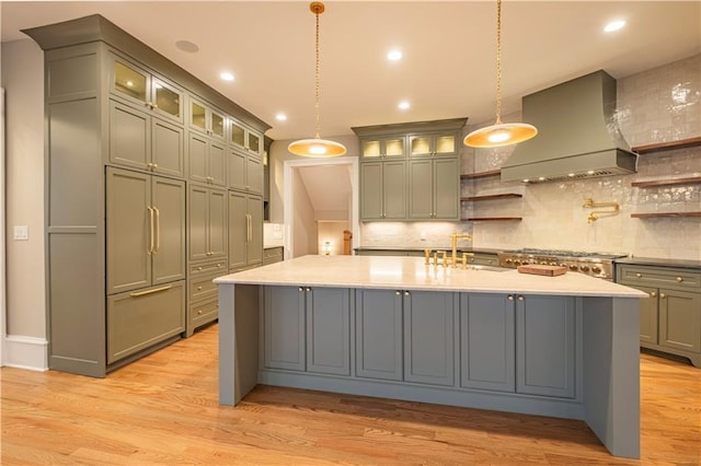 kitchen featuring a sink, a kitchen island with sink, light countertops, backsplash, and custom exhaust hood