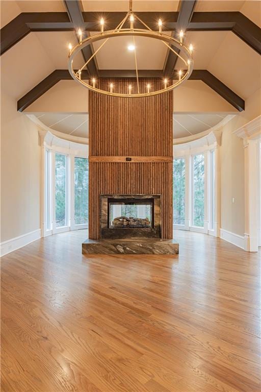 unfurnished living room with a multi sided fireplace, baseboards, an inviting chandelier, and wood finished floors