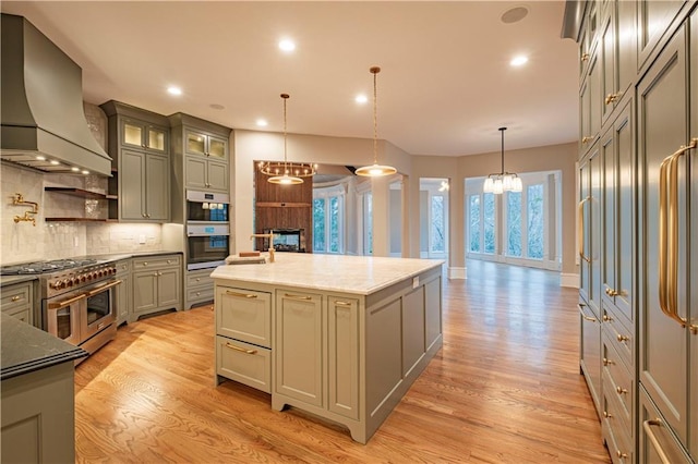 kitchen featuring a fireplace, custom range hood, gray cabinetry, light wood finished floors, and stainless steel appliances