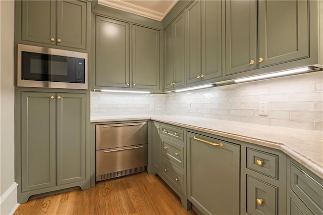 kitchen with light countertops, light wood-style flooring, stainless steel microwave, and backsplash
