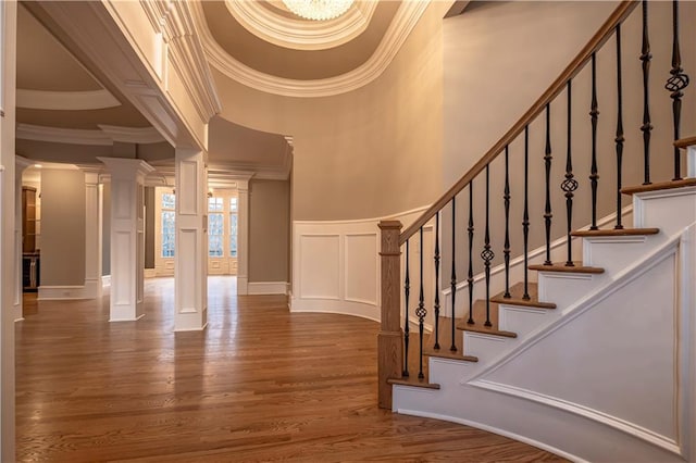 staircase with decorative columns, wood finished floors, a wainscoted wall, ornamental molding, and a decorative wall