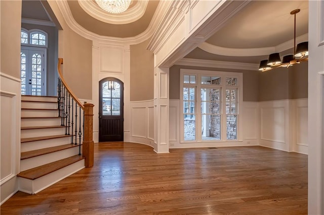 foyer entrance with stairway, a decorative wall, wood finished floors, and a notable chandelier