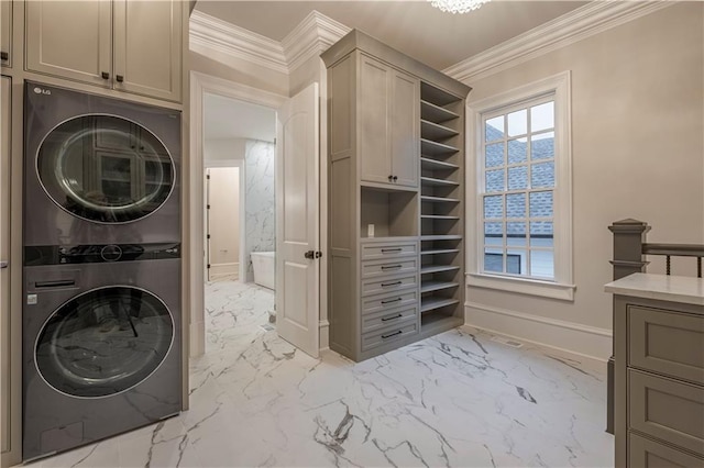 clothes washing area featuring cabinet space, marble finish floor, baseboards, stacked washer / dryer, and ornamental molding