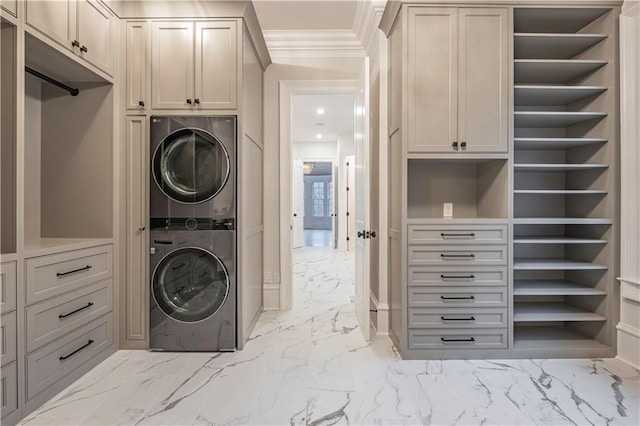 laundry area featuring ornamental molding, cabinet space, stacked washer / dryer, and marble finish floor