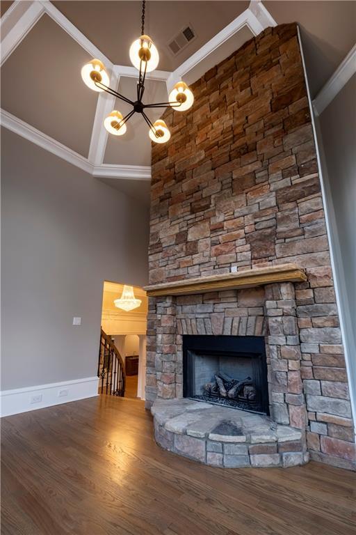 unfurnished living room featuring an inviting chandelier, baseboards, wood finished floors, visible vents, and ornamental molding