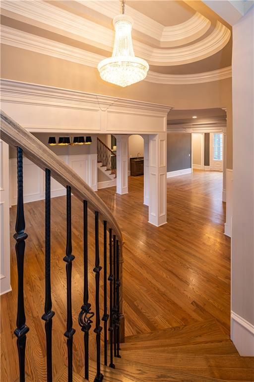 stairs featuring arched walkways, ornamental molding, wood finished floors, and a raised ceiling