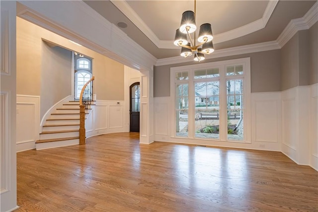 interior space featuring stairs, a decorative wall, a notable chandelier, and wainscoting
