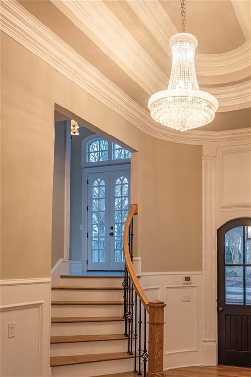 entrance foyer featuring wainscoting, a decorative wall, a chandelier, stairs, and ornamental molding