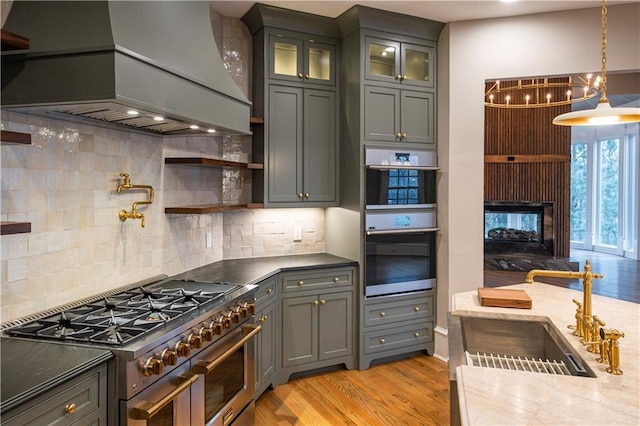 kitchen featuring tasteful backsplash, custom range hood, a sink, light wood finished floors, and appliances with stainless steel finishes
