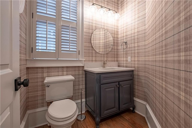 half bath featuring vanity, toilet, wallpapered walls, and wood finished floors