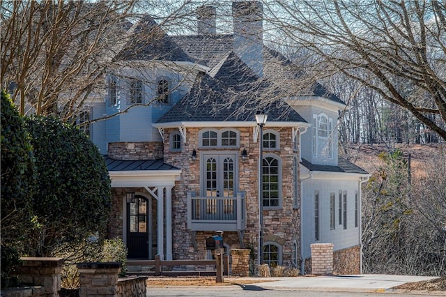 view of front of house with a standing seam roof, a chimney, fence private yard, and stone siding