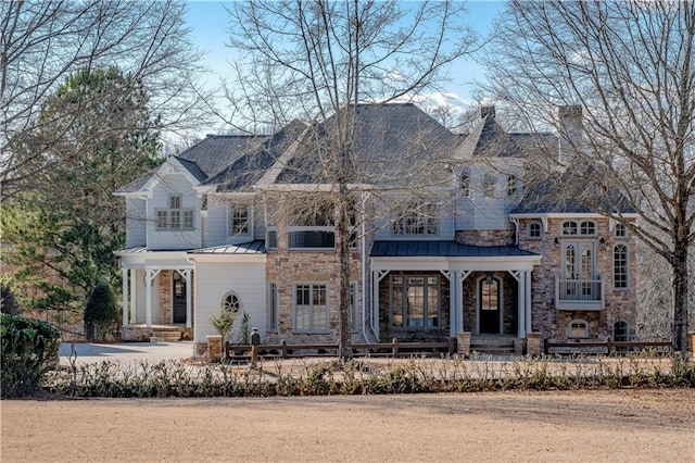 french country home featuring a standing seam roof, covered porch, a fenced front yard, and stone siding
