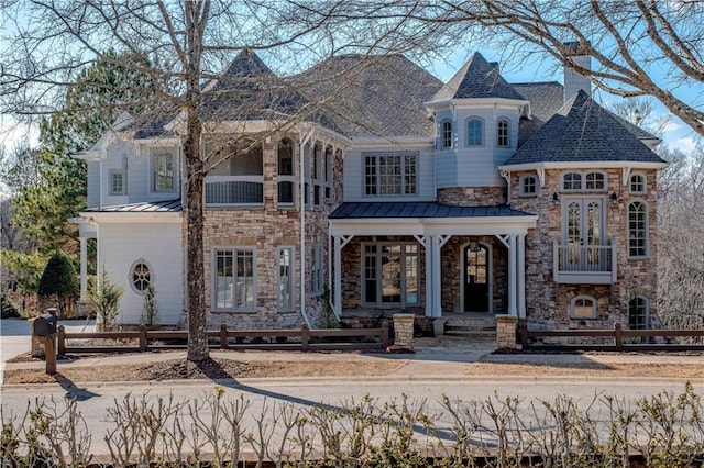 view of front facade with fence, a standing seam roof, a chimney, and stone siding