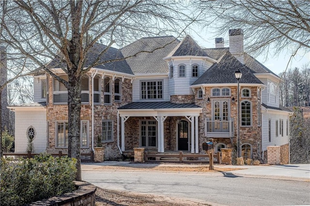 view of front facade with a standing seam roof, a chimney, a shingled roof, and stone siding
