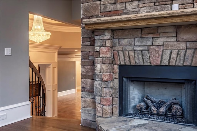 details featuring a stone fireplace, crown molding, wood finished floors, baseboards, and a chandelier