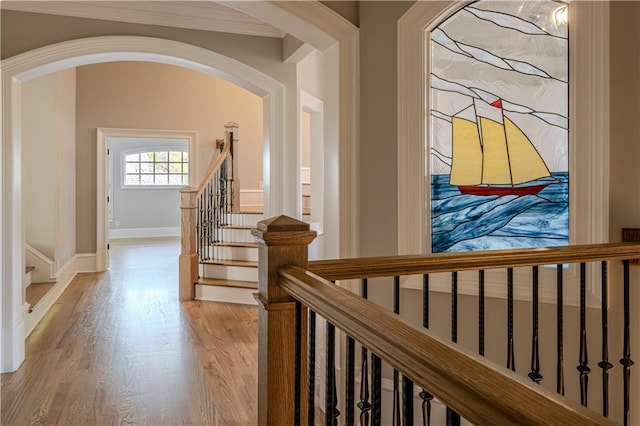 hallway featuring ornamental molding, wood finished floors, baseboards, stairway, and arched walkways