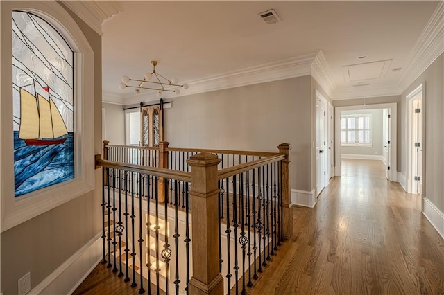 hallway featuring crown molding, visible vents, wood finished floors, baseboards, and attic access