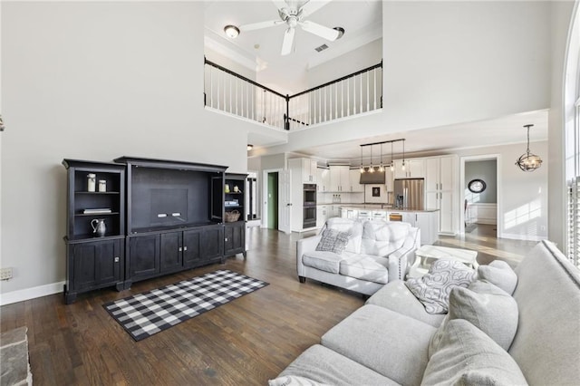 living room with dark hardwood / wood-style flooring, ceiling fan with notable chandelier, and a high ceiling