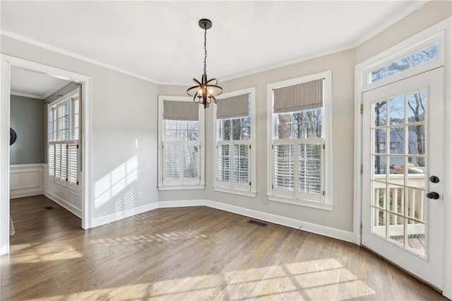 unfurnished dining area featuring crown molding, wood-type flooring, and an inviting chandelier