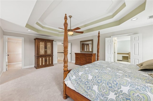 carpeted bedroom featuring a walk in closet, ornamental molding, a tray ceiling, a closet, and ceiling fan