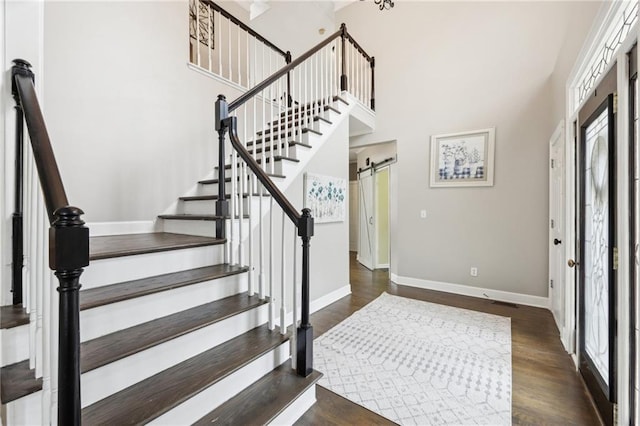 foyer featuring dark hardwood / wood-style floors, a barn door, a healthy amount of sunlight, and a towering ceiling