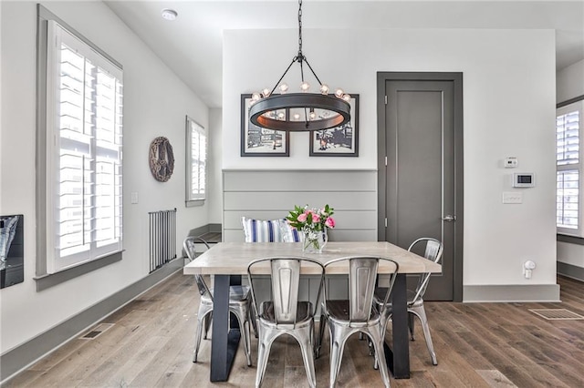 dining area featuring baseboards, visible vents, a chandelier, and wood finished floors