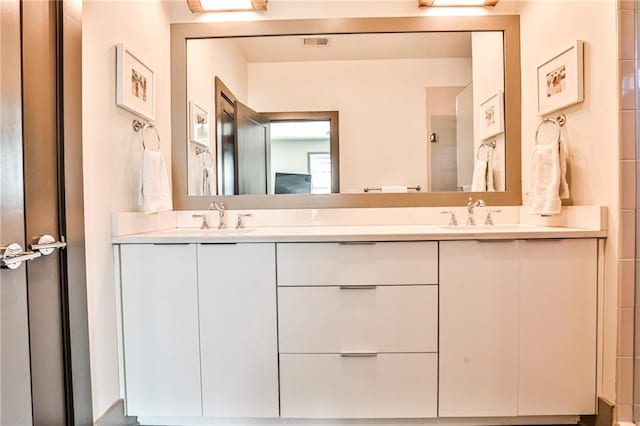 bathroom featuring double vanity, walk in shower, a sink, and visible vents