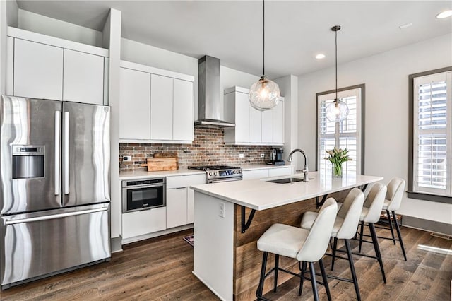 kitchen with tasteful backsplash, wall chimney exhaust hood, a breakfast bar, stainless steel appliances, and a sink