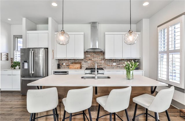 kitchen with a sink, backsplash, wall chimney exhaust hood, modern cabinets, and stainless steel fridge