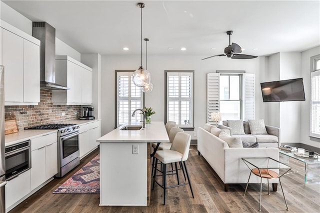 kitchen with wall chimney exhaust hood, a breakfast bar area, dark wood-style flooring, stainless steel appliances, and a sink