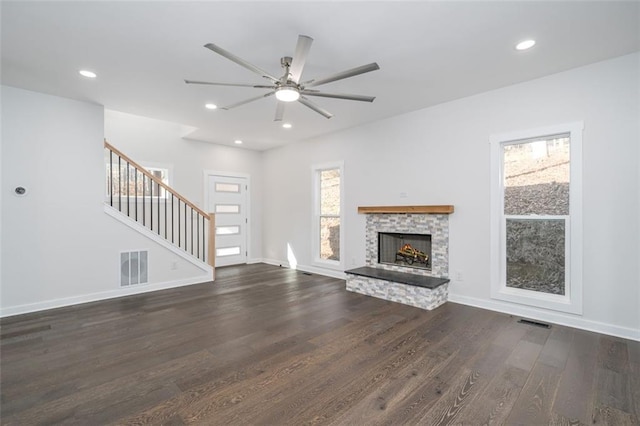 unfurnished living room featuring dark hardwood / wood-style floors, ceiling fan, and a stone fireplace