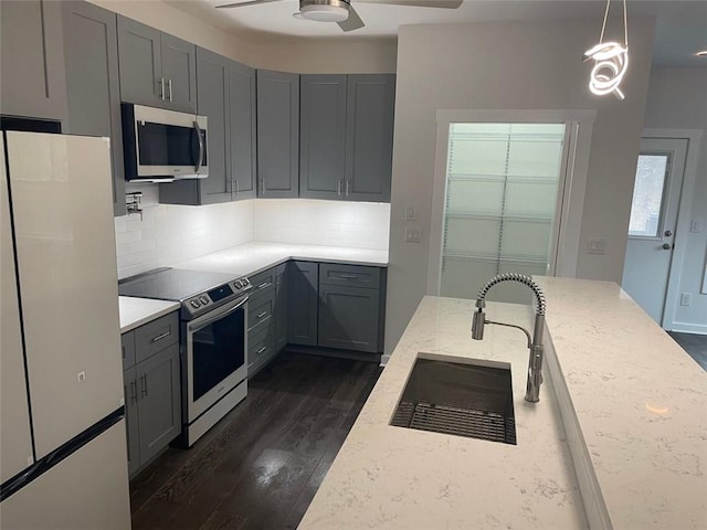 kitchen featuring gray cabinetry, dark hardwood / wood-style floors, appliances with stainless steel finishes, decorative light fixtures, and light stone counters