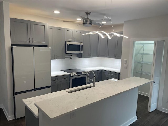 kitchen with sink, ceiling fan, gray cabinets, light stone countertops, and appliances with stainless steel finishes