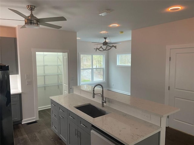 kitchen featuring dark wood-type flooring, sink, stainless steel dishwasher, a kitchen island, and light stone counters