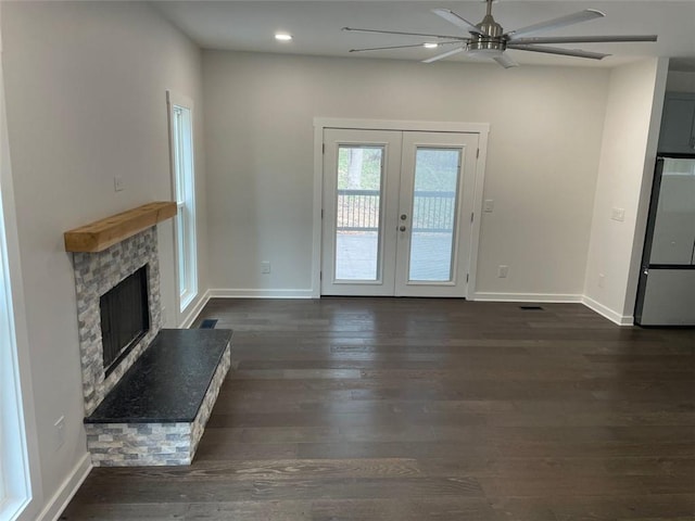 unfurnished living room with a stone fireplace, ceiling fan, french doors, and dark hardwood / wood-style floors