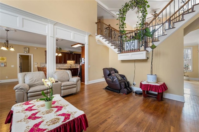 living area featuring baseboards, stairway, wood finished floors, crown molding, and a chandelier