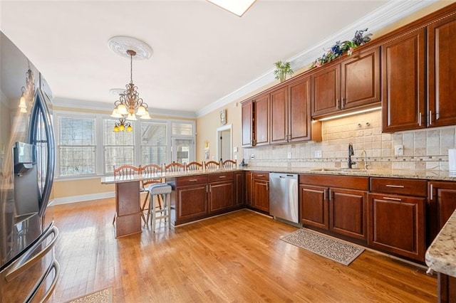 kitchen with light wood-style flooring, stainless steel appliances, a peninsula, a sink, and ornamental molding