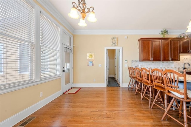 dining room with crown molding, visible vents, an inviting chandelier, light wood-style floors, and baseboards