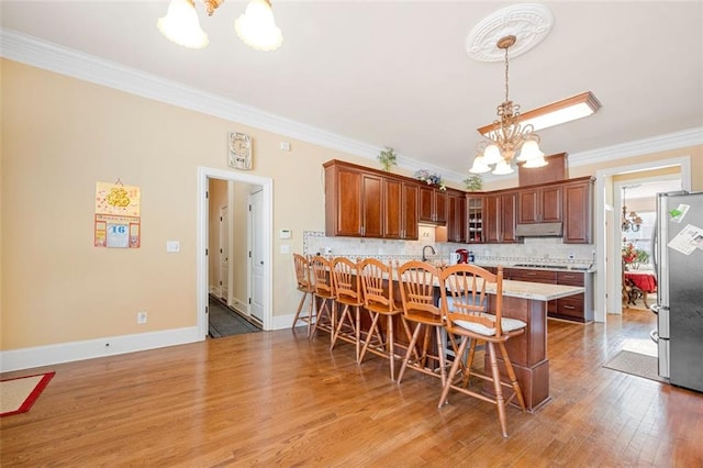 kitchen with under cabinet range hood, ornamental molding, freestanding refrigerator, decorative backsplash, and an inviting chandelier