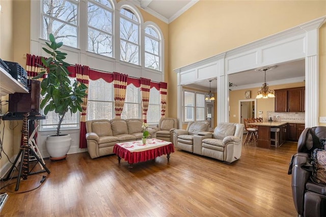 living area featuring light wood finished floors, a high ceiling, a chandelier, and crown molding