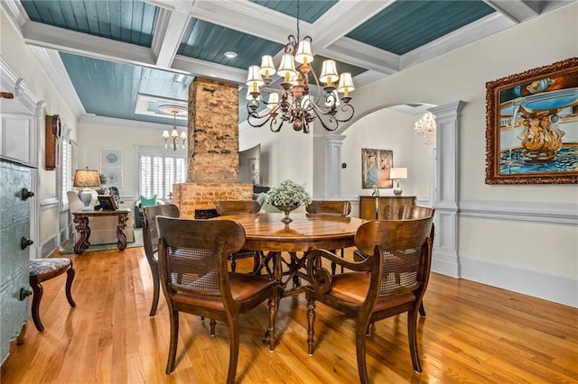 dining area with light wood finished floors, coffered ceiling, ornate columns, arched walkways, and a notable chandelier