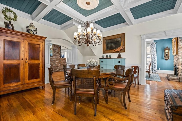 dining room with a notable chandelier, coffered ceiling, wood finished floors, arched walkways, and ornate columns