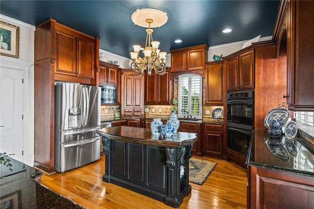 kitchen with decorative backsplash, dark stone countertops, wood finished floors, a notable chandelier, and stainless steel appliances