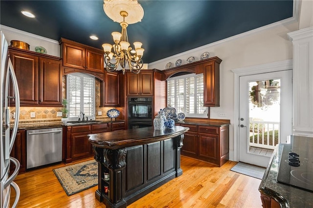 kitchen featuring light wood-style flooring, a sink, backsplash, stainless steel appliances, and a chandelier