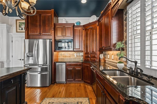 kitchen with dark stone counters, a sink, light wood-style floors, black microwave, and stainless steel fridge