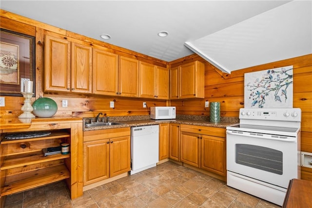 kitchen with brown cabinetry, wood walls, white appliances, and a sink