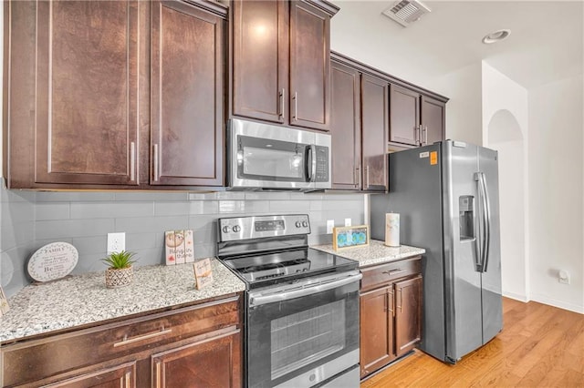 kitchen with light stone countertops, backsplash, appliances with stainless steel finishes, and light wood-type flooring